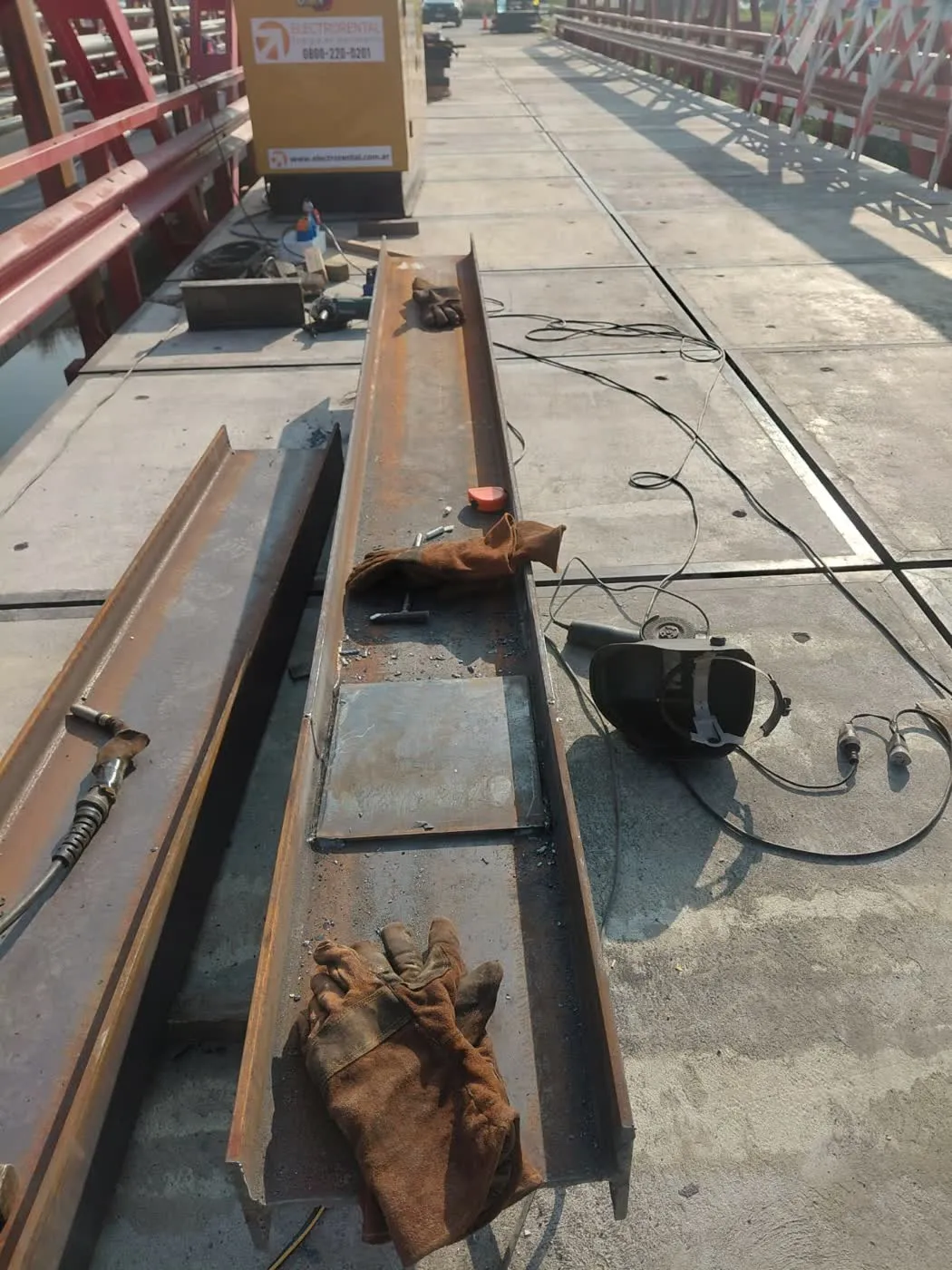 Operarios trabajando sobre estructura de puente metálico a la vera de un río